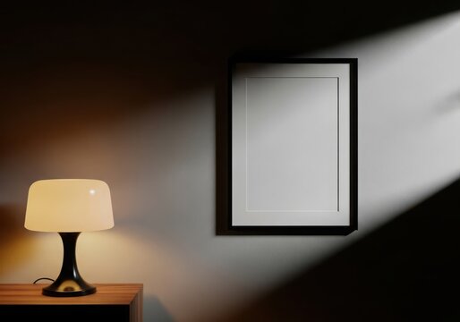 Empty vertical black picture frame hanging on a dark wall with a glowing table lamp and natural light beam in a room