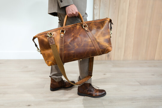 Waist down side view of a man in a suit Holding a Brown Leather Bag