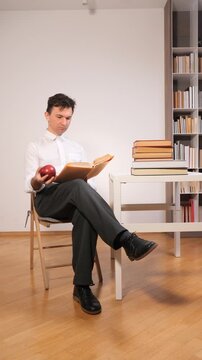 Vertical video man reading book while considering the concept of gravity and physics with an apple levitating above his hand in a modern intellectual setting