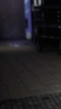 People walk on the floor next to vending machines in a dark hallway. The lights create shadows, and the area seems quiet with an empty atmosphere.