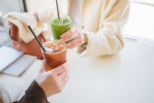 Close up of two women sitting at a table clinking glasses of iced matcha latte and espresso tonic