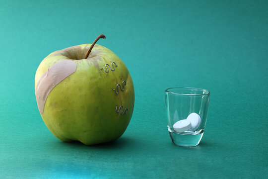 Still life of injured apple with band-aid, clamps and medicaments. Photo with great depth of field on green background.
