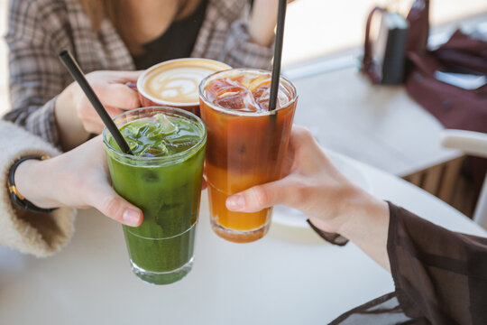Close-up of three women sitting at a table clinking glasses of iced matcha latte, espresso tonic and a cappuccino