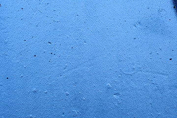 Rough blue concrete wall with a small black spray paint stain in one corner © DavidIgSu