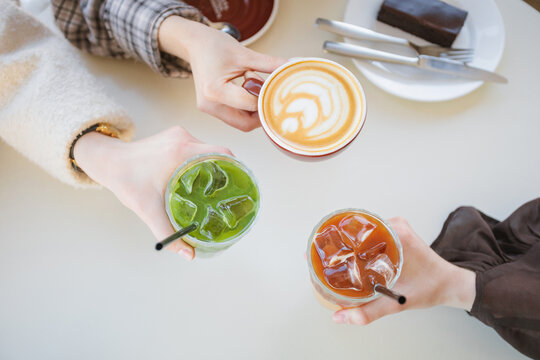 Overhead view of three women sitting at a table clinking glasses of iced matcha latte, espresso tonic and a cappuccino