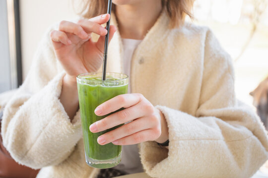 Close-up Portrait of a young woman sitting in a cafe drinking a glass of iced matcha latte through a straw