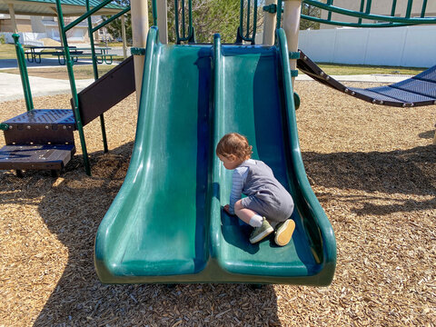 Rear view of a young boy sitting on a slide in a playground on a summer day, Riverton, Utah, USA