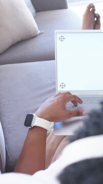 Vertical video: Placing laptop on lap leading man in shorts typing on sofa, crop marks on screen