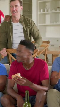 Vertical video: Eating bun, red-tee man giving slap after pal pumping fist in game on sofa with pad