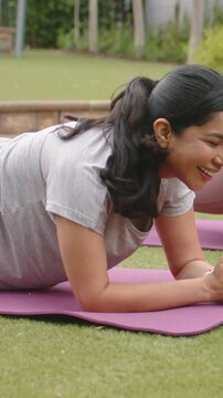 Vertical video: Reacting to buzz, woman in grey tee holding forearm plank on purple mat in yard