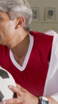 Vertical video: Reacting man in red tee holding football on sofa as friend pointing watching match