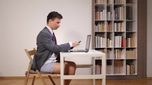 Businessman in suit jacket, tie and boxer shorts sits at home desk on a video call, laptop openhumorous take on remote work, virtual meetings and work from home life