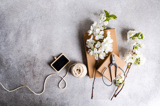 Overhead view of cherry blossom branches on two cardboard gift boxes with a blank chalkboard, string and scissors
