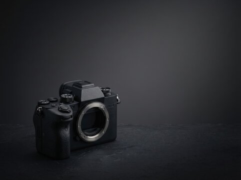 Black mirrorless camera body placed on dark textured surface for modern product background and equipment presentation or promotional banner