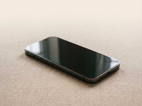 Modern smartphone with reflective glass screen lying on beige fabric for minimalist mockup background and device presentation or wallpaper design