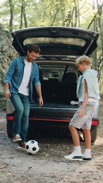 Father play football with cute son have fun kicking soccer ball mother and daughter are preparing food for a picnic. Happy parents and children play family kids games together in nature. Slow motion.