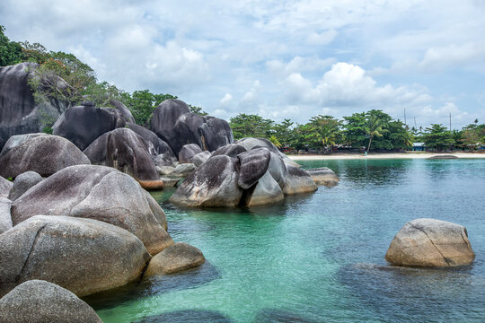Large granite boulders and lush trees on Tanjung Tinggi beach on an overcast day, Belitung Island, Indonesia