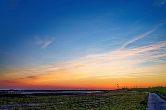 Distant view of a road leading to wind turbines along the river Ems at sunset, Petkum, East Frisia, Lower Saxony, Germany