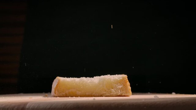 Slices of freshly baked bread falling onto a wooden board against a black background. Concept of baking, culinary arts, and food photography, ideal for use in gastronomy and lifestyle magazines.