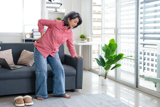 Hurt senior woman stand from couch touch back with pain, sick mature female struggle with backache painful ,  elderly healthcare concept