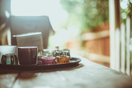 Close-up of assorted glasses and cups on a tray on a wooden table on a sunny day