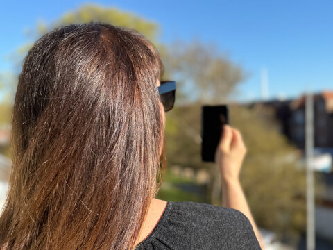 Rear view of a woman wearing sunglasses on a spring day standing outdoors using a mobile phone
