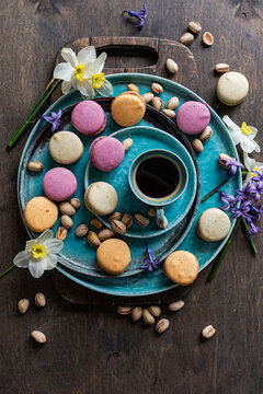 Close-up overhead view of a cup of black coffee with assorted macarons, pistachio nuts and spring flowers on ceramic crockery on a wooden table