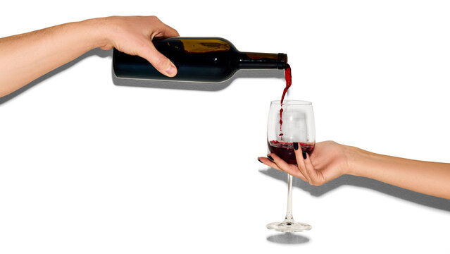 Hand pouring red wine into glass isolated on white background with copy space. Concept of celebration, luxury lifestyle, beverage promo, restaurant menu design and social drinking mood.