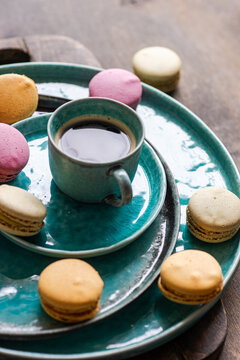 Close-up of a cup of black coffee with assorted macarons on a stack of assorted ceramic crockery on a wooden chopping board and table