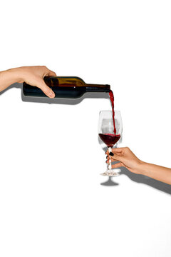 Minimal composition of hands pouring red wine into glass on white background. Concept of modern beverage advertising, copy space design, hospitality service and elegant lifestyle.