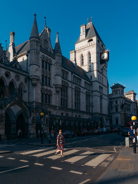 View of an ornate grey stone building with a clock tower under a blue sky, contrasting with a person on a zebra crossing, London, England, United Kingdom.
