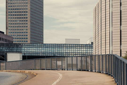 Railing and concrete architecture shape an empty urban bridge walkway with modern office backdrop on a curve creating contemplative city passage