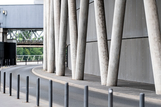 Concrete pillars in an urban underpass curve along empty street with sidewalk bollards and sparse infrastructure creating minimalist transit corridor
