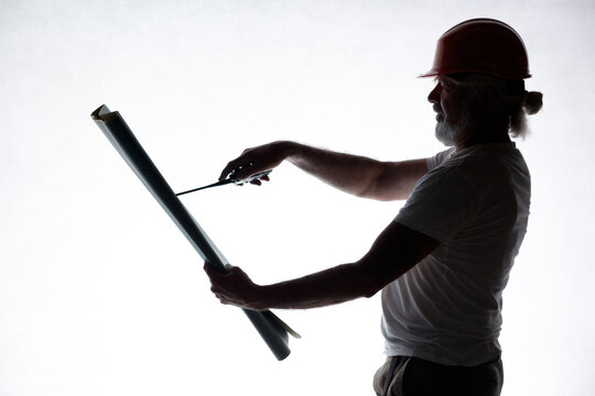 Profile of a mature construction supervisor communicating instructions and checking project plans with a radio antenna. Backlit studio shot