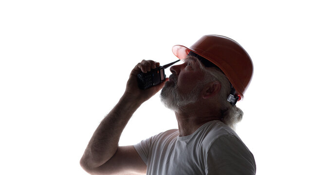 Silhouette of a senior construction worker in a hard hat talking on a walkie-talkie, isolated on a white background