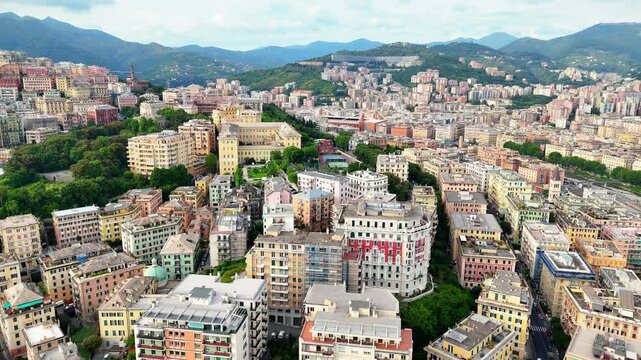 Aerial drone flyover of Genoa city with dense colorful architecture and mountain backdrop, Italy.