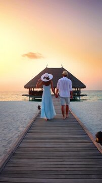 A romantic holiday couple walks down a wooden pier in the Maldives islands during sunset time