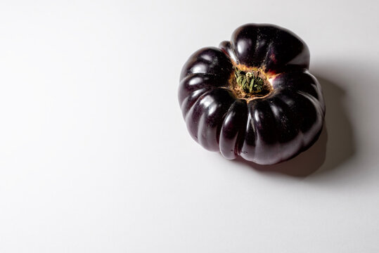 Un tomate morado de variedad antigua entero en el lado derecho de un fondo blanco con sombra suave. Toma desde un &aacute;ngulo alto con amplio espacio negativo para texto.