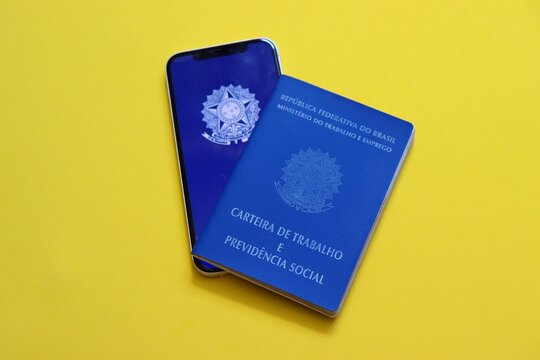 Salvador, Brazil - April 27, 2026: The traditional blue Brazilian Work Permit (CTPS) next to a smartphone displaying the Digital Work Card app. Carteira de Trabalho do Brasil (Brazilian Word Card). 