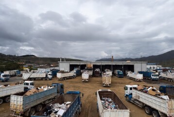 Fototapeta premium Recycling center with trucks full of waste and cardboard under a cloudy sky