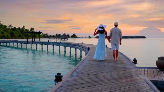 A couple walks holding hands over a pier in the tropical Maldives islands during their romantic vacations