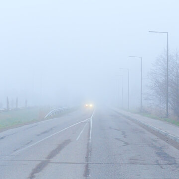 Car headlights glowing in thick white fog on an empty road, minimalist perspective