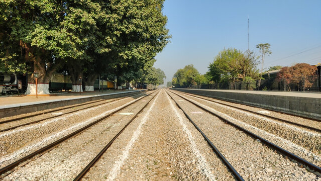 Railway tracks stretching forward on ballast stones at station in daylight with travel direction mood