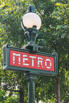Paris, France. May 14, 2025, Ornate green metro sign with red background and white letters stands tall against lush green trees in Paris