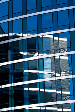 Blue modern glass facade of a curved building where reflection follows smooth curves creating an abstract pattern in contemporary architecture detail