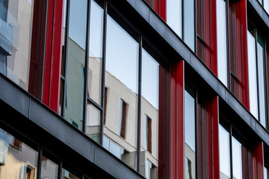 Red panels on a modern urban building facade with windows create bold geometry pattern and graphic lines in contemporary architecture detail