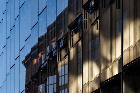 Urban modern architecture of a glass building facade with windows in shadow creating strong contrast and layered reflection across the surface