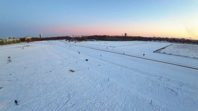 Aerial FPV view of the vast, snow-covered Tempelhofer Feld with faint tracks, bathed in soft twilight hues, Berlin, Berlin, Germany.
