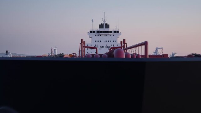 Camera flies towards and over an anchored crude oil super tanker to reveal more anchored ships. Aerial view of anchored oil tankers at sunset. Strait of Hormuz blockade concept. 3d animation render