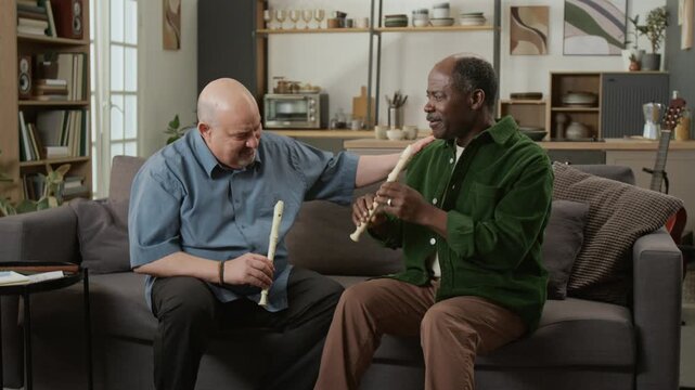 Front view shot of teacher giving praise to adult African American man learning recorder and patting him on shoulder smiling while sitting on sofa together Useful for coaching services